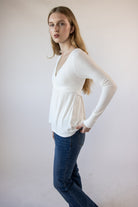 Model wearing a white ribbed crossover long-sleeve top and blue jeans