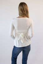 Back view of a woman wearing a white ribbed long-sleeve top with a back tie waist and blue jeans