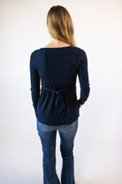 Back view of a woman wearing a navy blue long-sleeve polka dot top with a waist tie and blue jeans