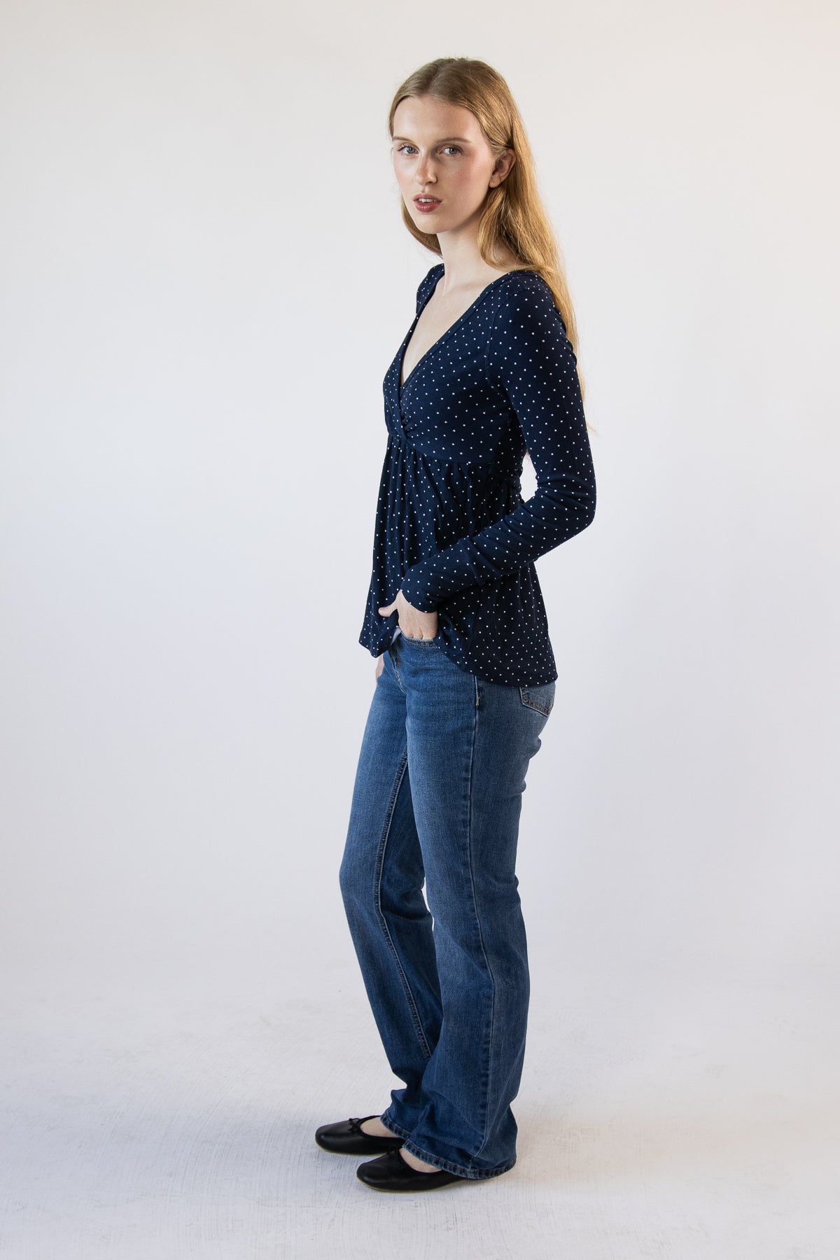 Woman wearing a navy blue polka dot long-sleeve V-neck top paired with blue jeans