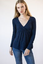 Woman wearing a navy blue polka dot long-sleeve top with a V-neck and empire waist