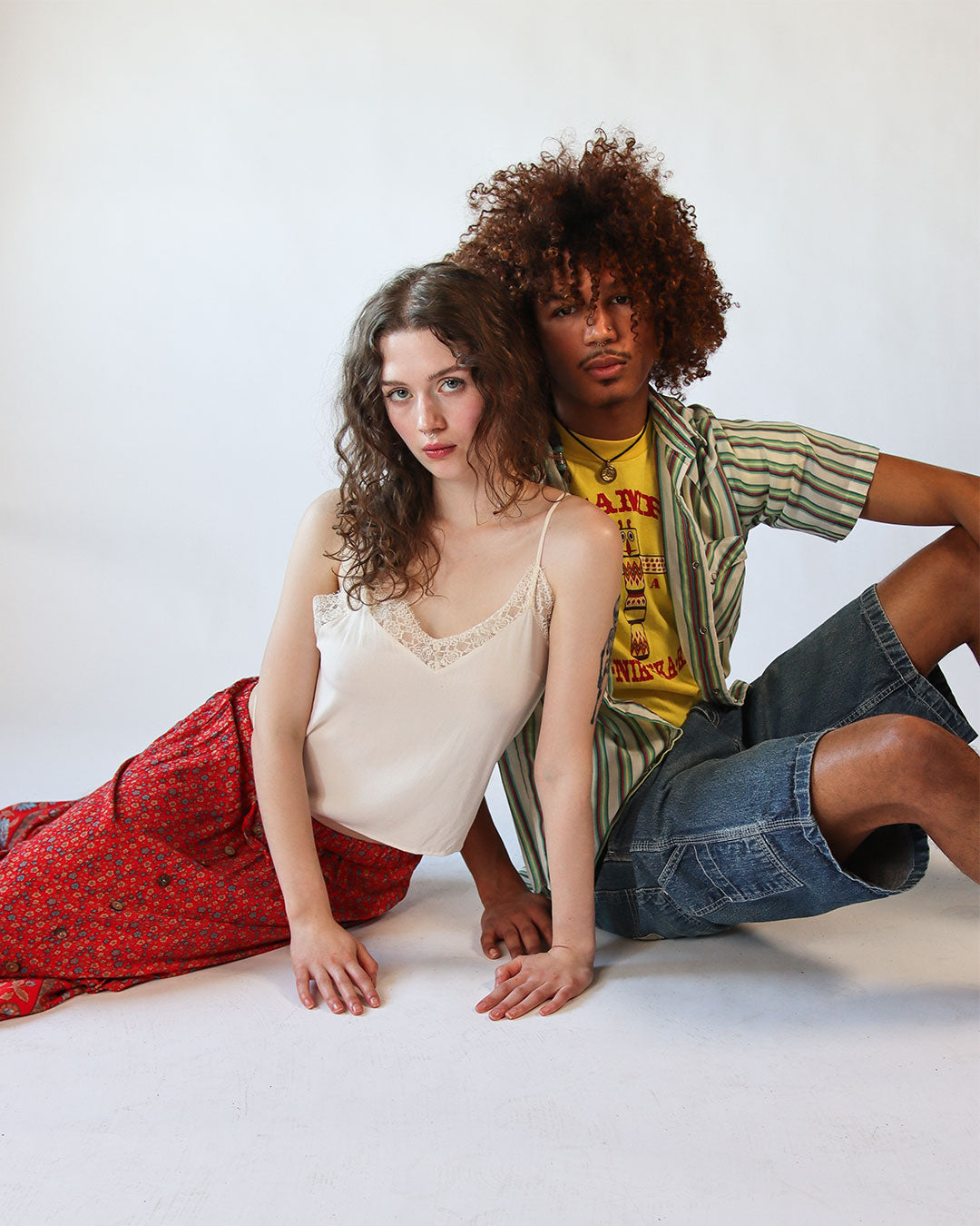 Two people sitting on a white floor against a white wall.