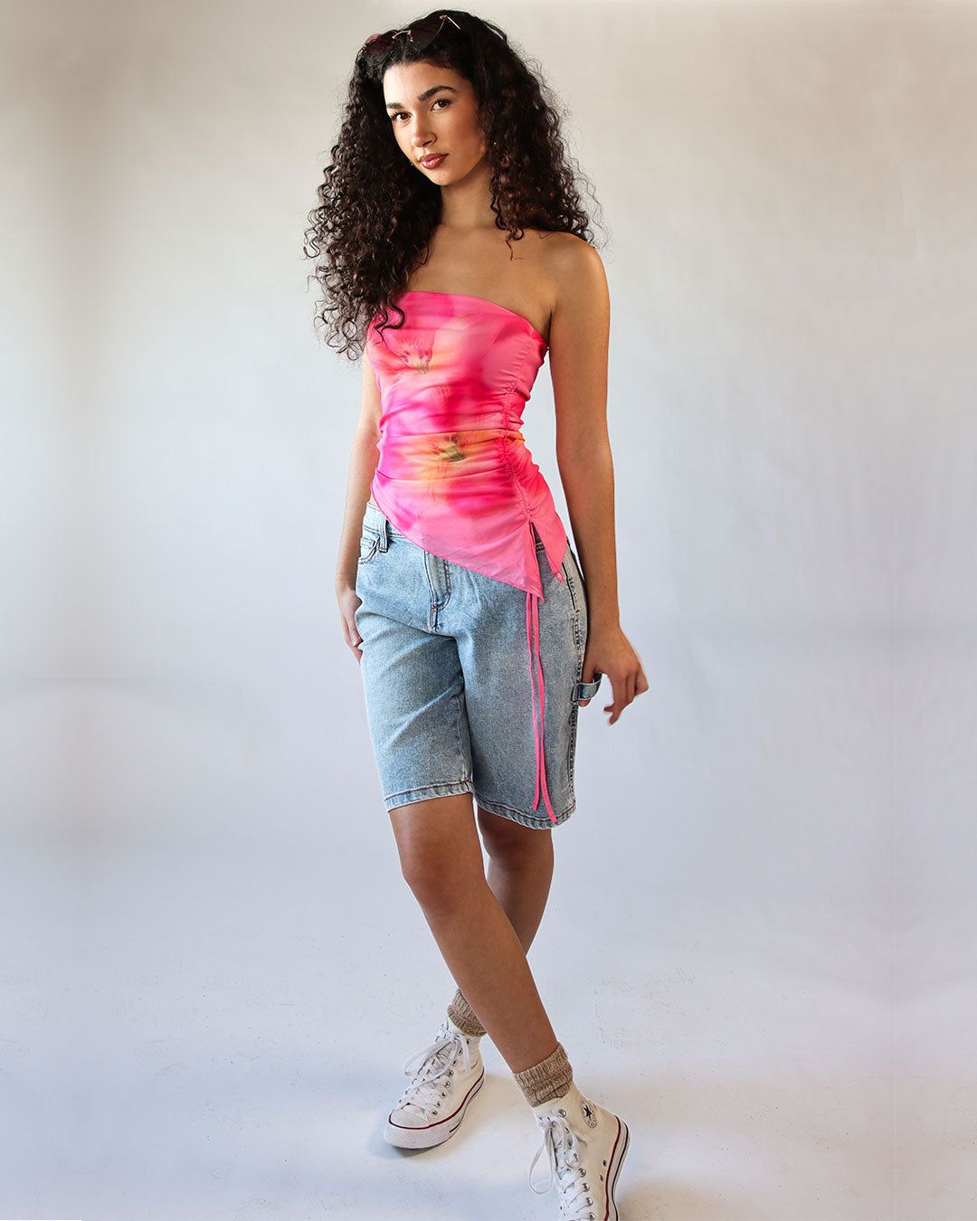 Woman wearing a pink strapless top and denim shorts on a plain background