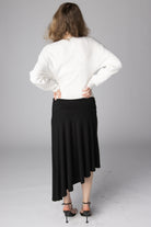 Back view of a woman wearing a white ribbed sweater and a black asymmetrical midi skirt
