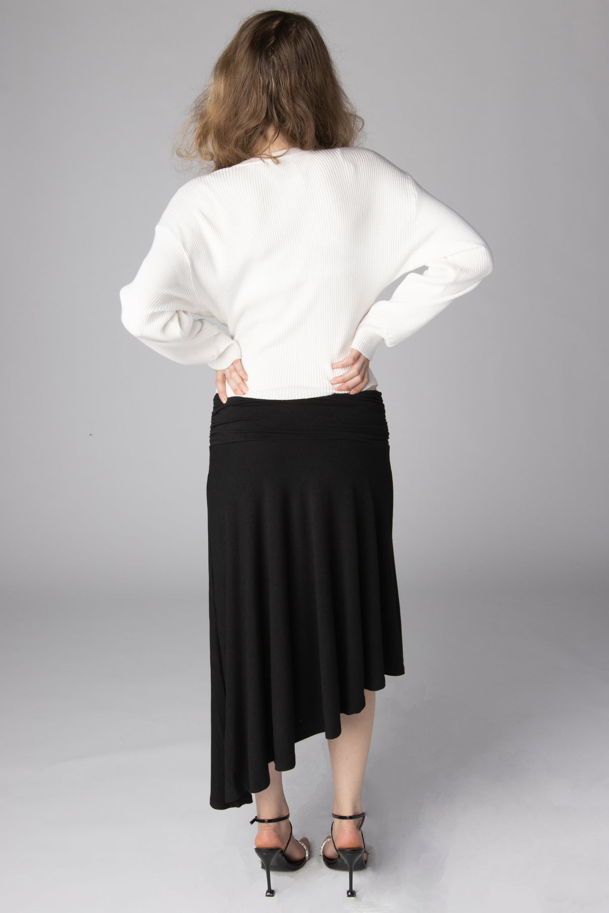 Back view of a woman wearing a white ribbed sweater and black asymmetrical midi skirt