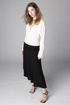 Woman wearing a white V-neck wrap sweater and a black midi skirt paired with strappy heels