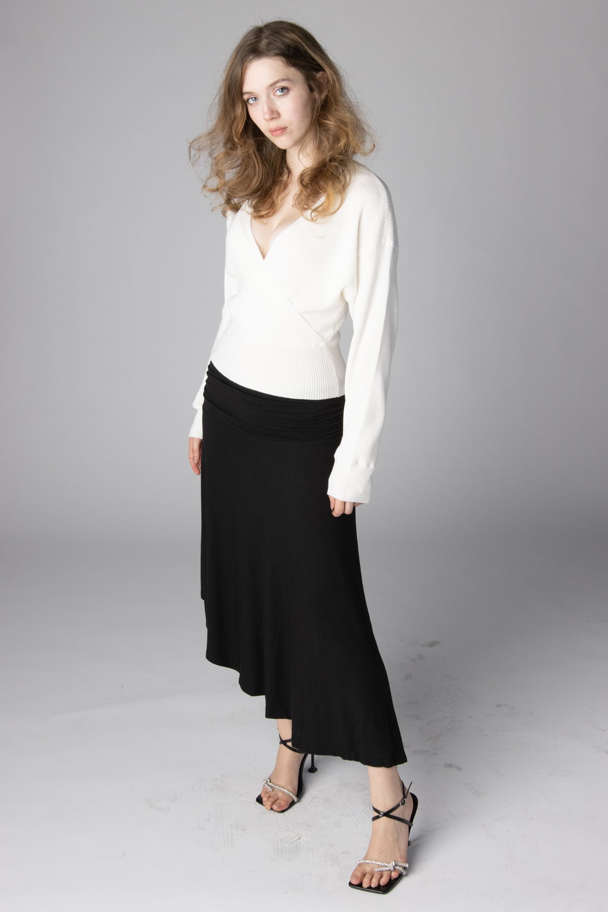 Woman wearing a white V-neck wrap sweater and a black midi skirt paired with strappy heels
