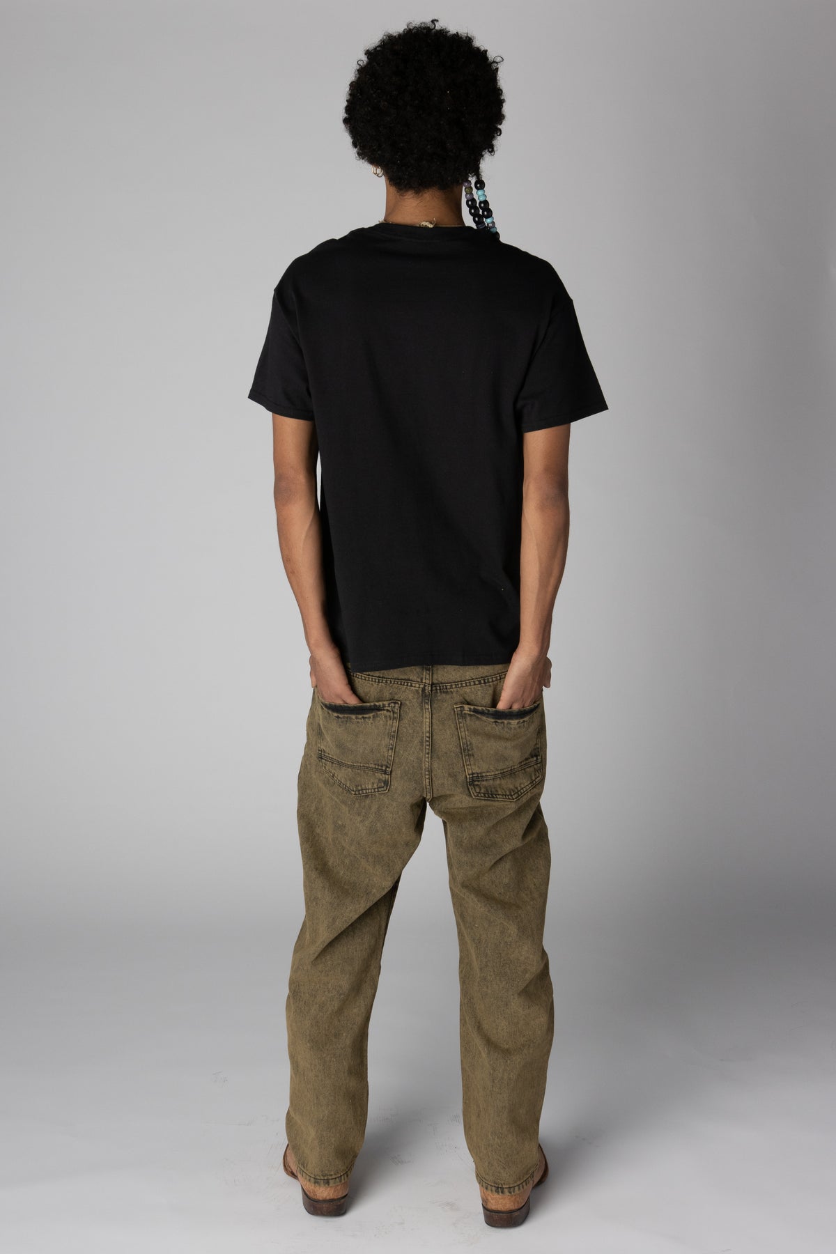 Back view of a person wearing a plain black t-shirt and acid-washed tan denim jeans