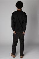 Back view of a person wearing a plain black crewneck sweatshirt and relaxed dark jeans