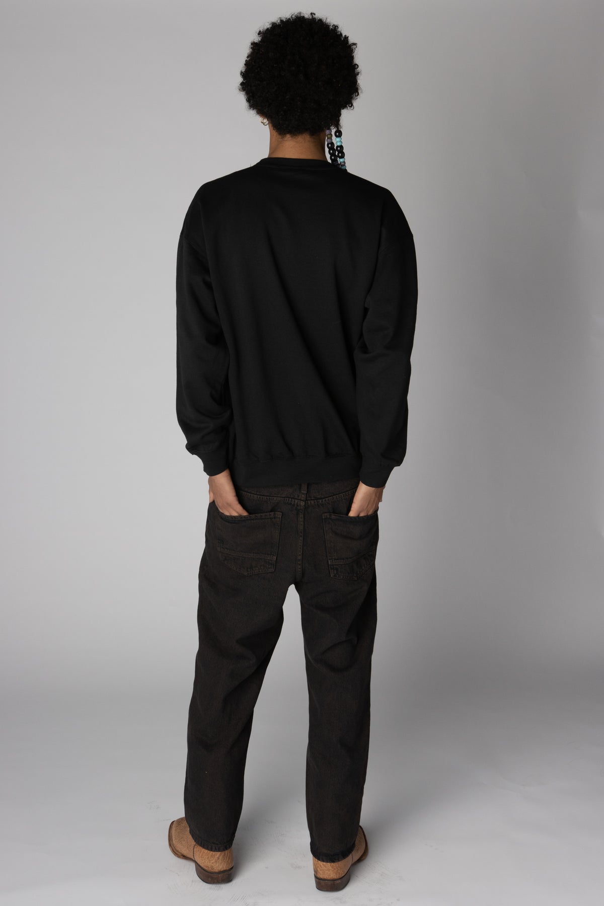 Back view of a person wearing a plain black crewneck sweatshirt and relaxed dark jeans