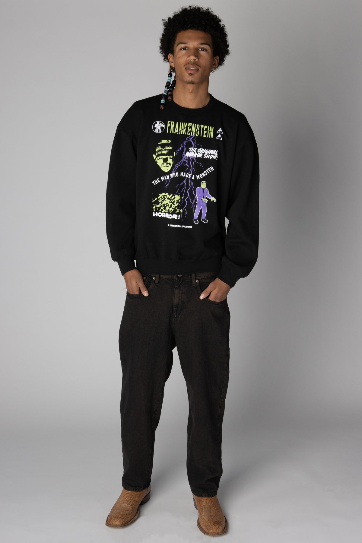 Man wearing a black crewneck sweatshirt featuring Frankenstein graphics with black jeans