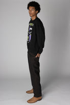 Side view of a man wearing a black Frankenstein graphic sweatshirt, dark jeans, and tan boots