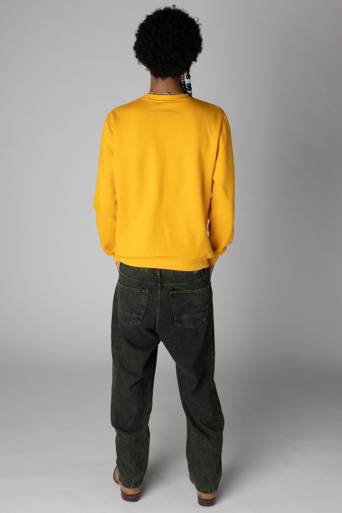 Back view of model wearing a bright yellow crewneck sweatshirt and relaxed-fit dark wash jeans