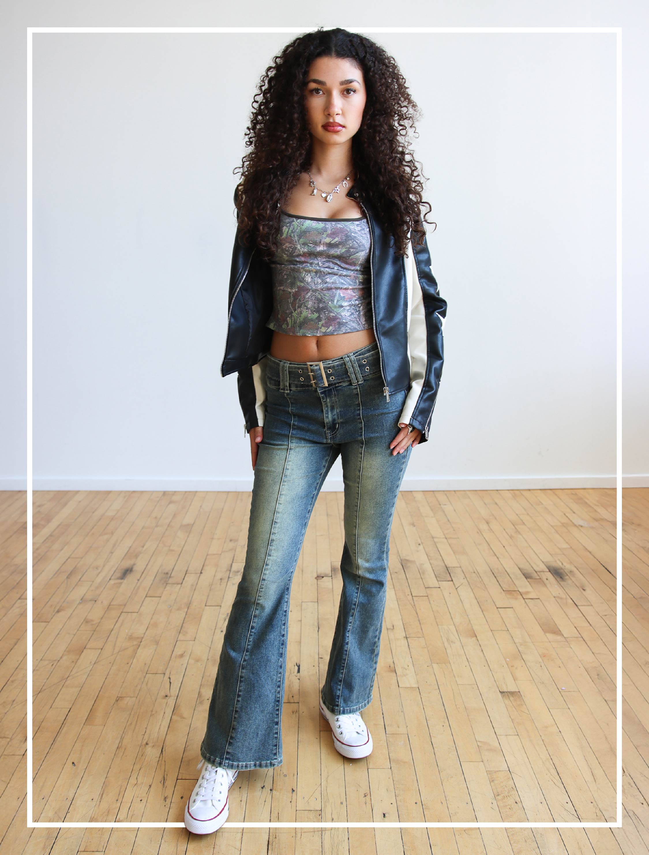 female model wearing woodland tank top, pleather moto jacket, and Y2K belted jeans.