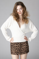 Woman wearing a white long-sleeve ribbed wrap sweater and a leopard print mini skirt