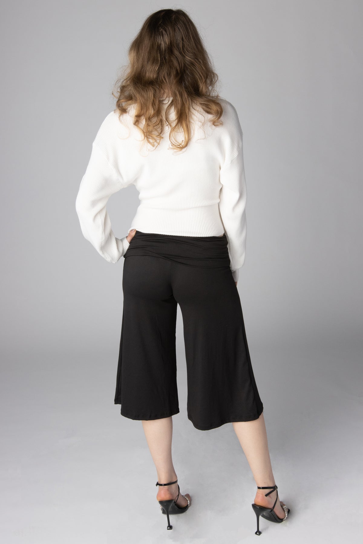 Back view of model wearing black cropped wide-leg pants with a fold-over waistband