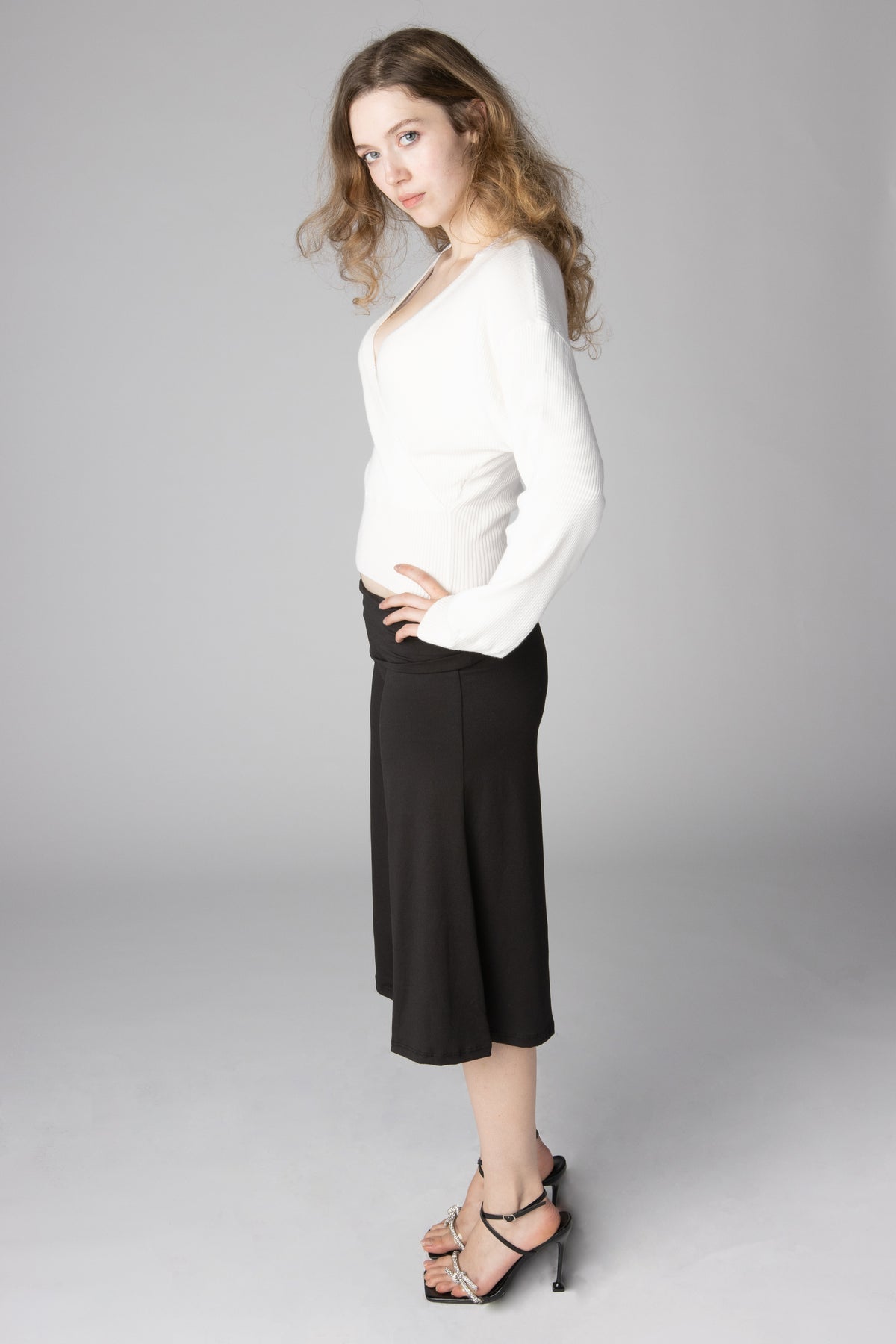 Woman modeling a white knit wrap top paired with a black midi skirt and embellished heels