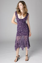 Woman modeling purple paisley print midi dress with ruffled scoop neck and handkerchief hem