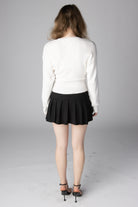 Model from behind wearing a white long-sleeve ribbed sweater and black pleated mini skirt