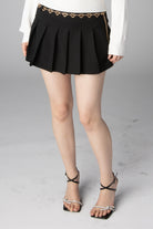 Black pleated mini skirt featuring a gold heart-shaped chain belt