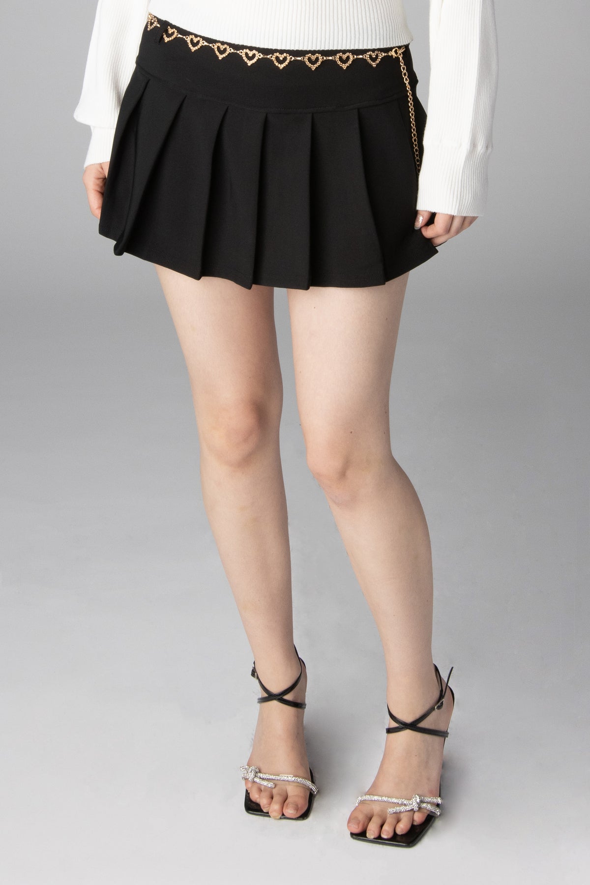 Black pleated mini skirt featuring a gold heart chain belt