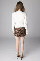 Back view of a woman wearing a white ribbed long-sleeve knit sweater and a leopard print mini skirt