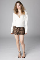 Woman wearing a white long-sleeve wrap sweater and a leopard print mini skirt with strappy heels