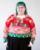 Person wearing a red, pink, and green holiday sweater with snowflakes and sparkly Merry Christmas lettering