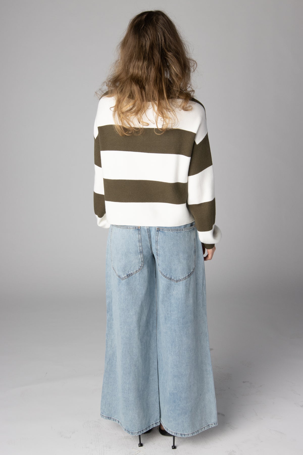 Back view of a woman wearing an olive green and white striped sweater paired with wide