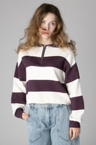 Woman wearing a cropped white and dark purple striped half-zip knit sweater with jeans
