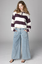Woman wearing a maroon and cream striped half-zip cropped sweater with light-wash wide-leg