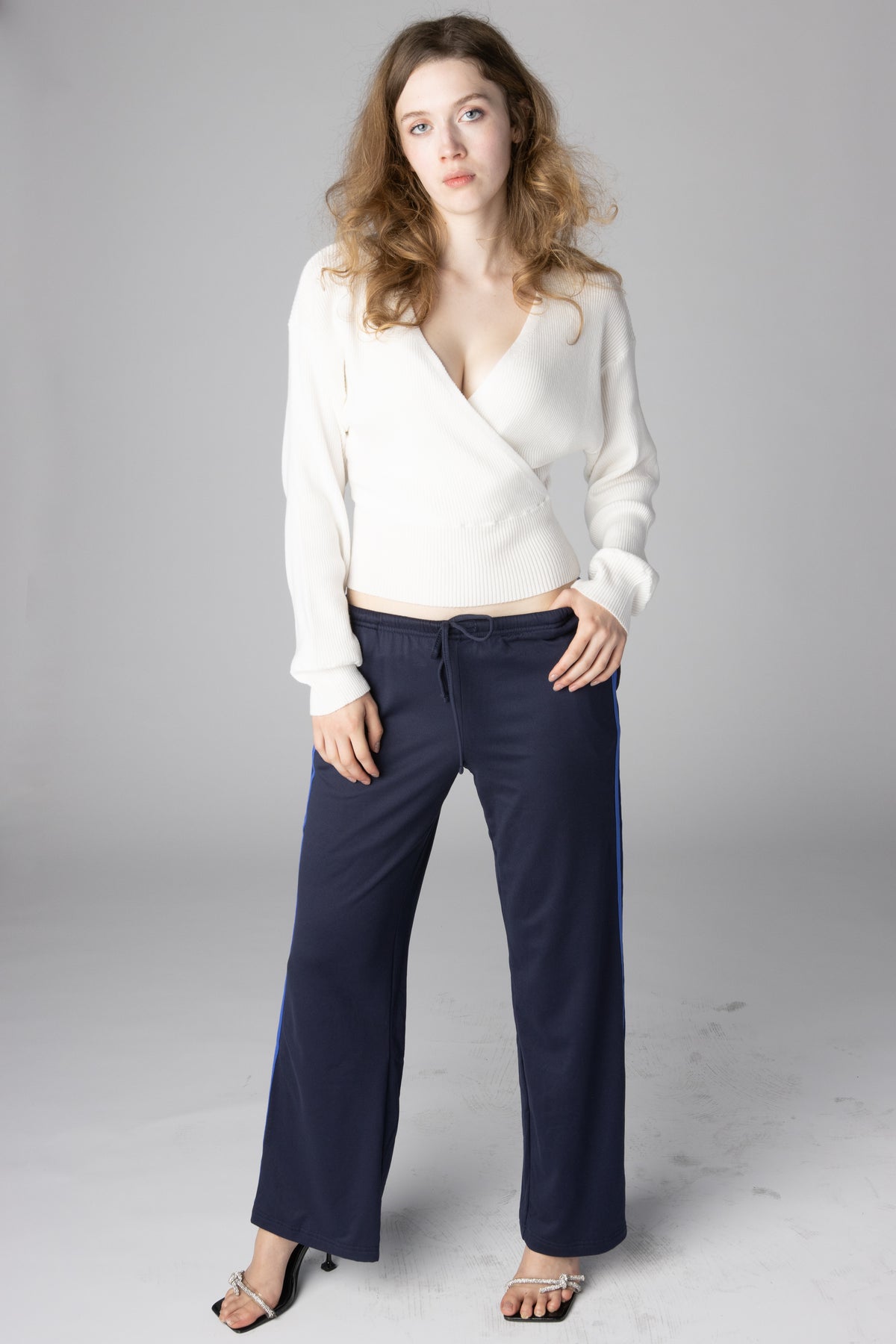 Woman wearing a white knit wrap sweater and navy blue track pants with side stripes