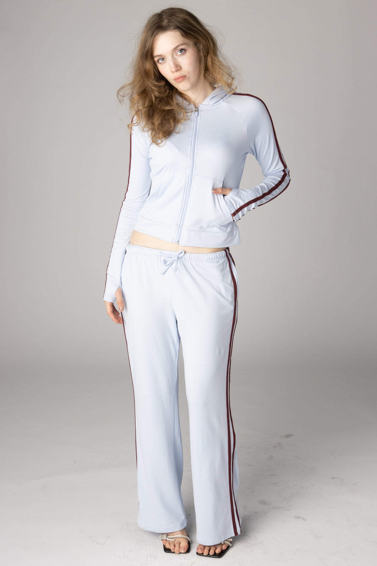 Woman modeling a light blue zip-up jacket and wide-leg track pants set with burgundy side stripes