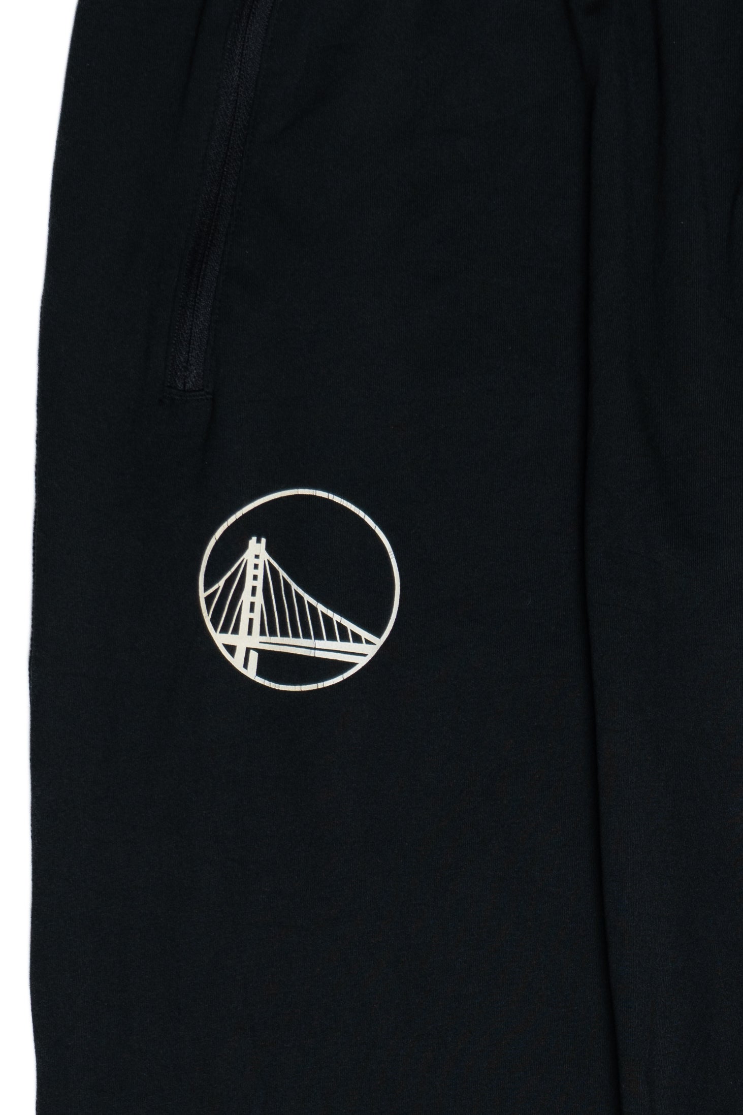 Close-up of black Nike Dri-FIT track pants with San Francisco bridge embroidered logo on thigh and zippered pocket detail.